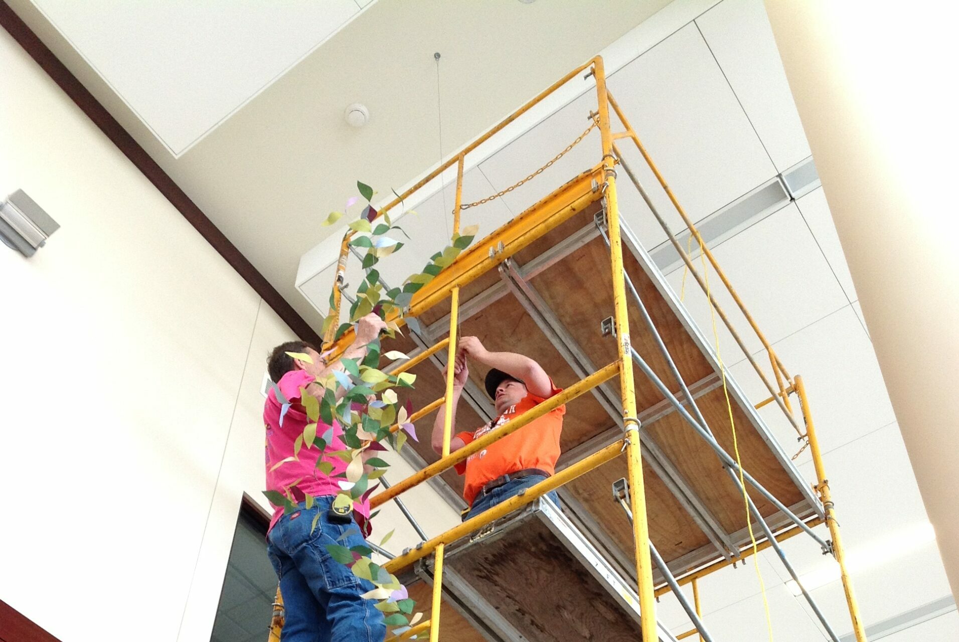 Two contactors hanging art pieces from scaffolding.